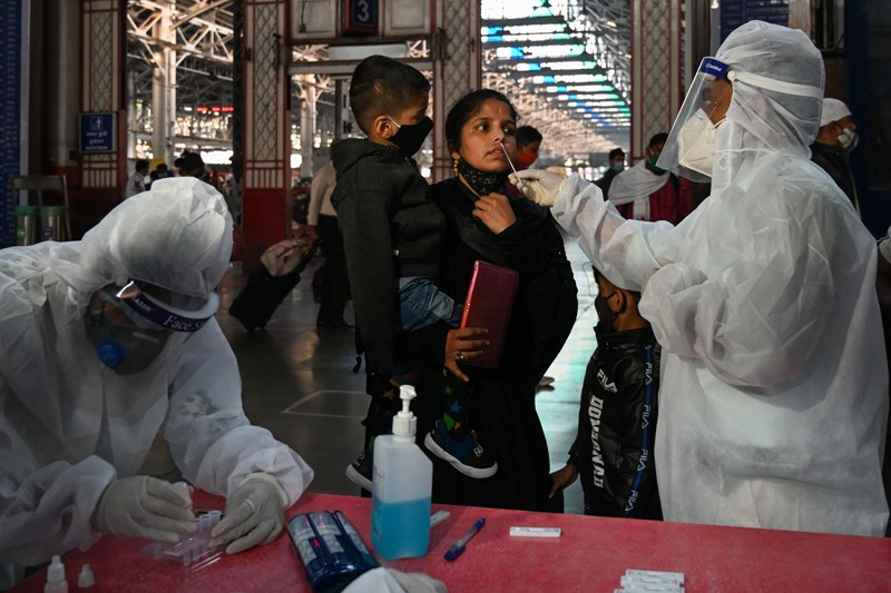 A health worker wearing protective suit takes a nasal swab of a woman holding a baby at a railway station in India