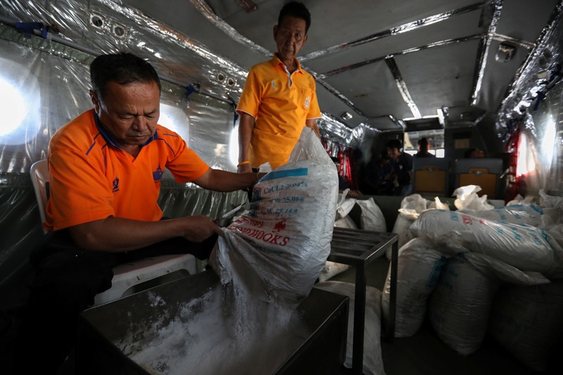 Workers pour chemicals as an aircraft flies over the outskirts of Bangkok