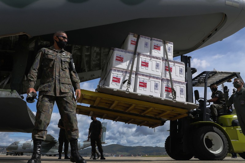 Military personnel unload large shipment of vaccines from the back of a cargo plane using a fork lift