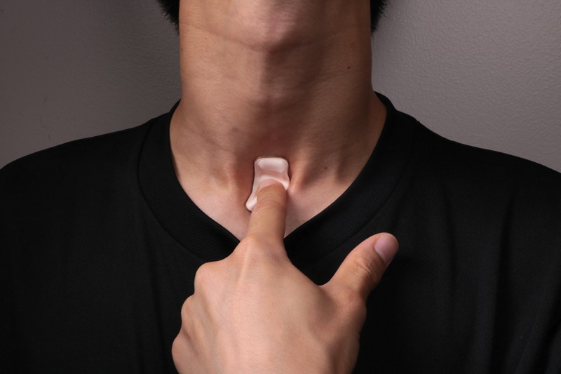 Close up of a man pressing his finger against a sticking plaster-like device attached to his throat