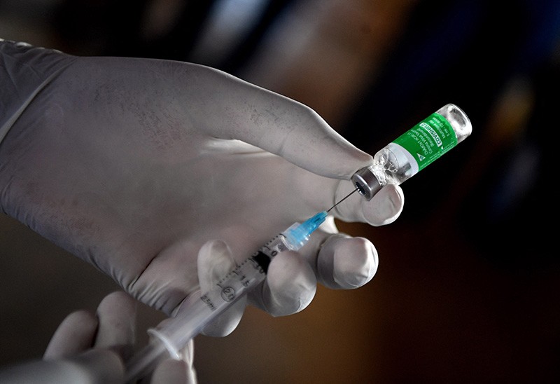 Close up of gloved hands filling a syringe from a bottle.