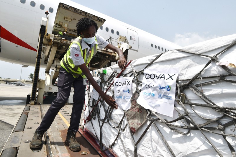 A worker adds a Covax sticker to a large shipment of Covid-19 vaccines unloaded from a plane in Ivory Coast