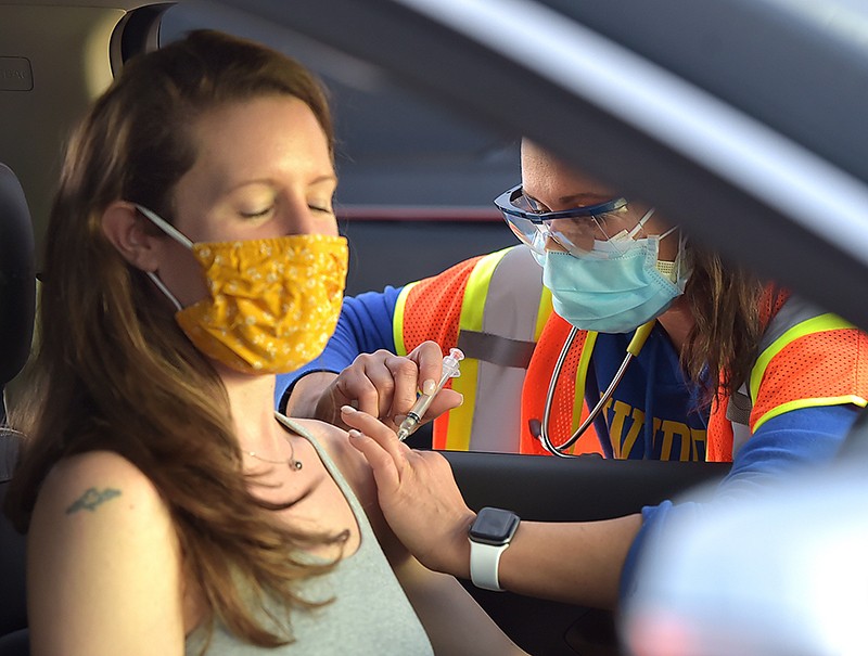 A masked person in a car receives an injection.