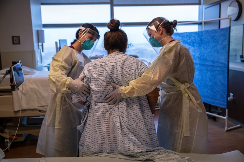 Hospital workers help a COVID-19 patient to stand up