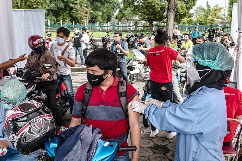 Healthcare workers administer the Sinovac Covid-19 vaccine to people on motorcycles in Indonesia