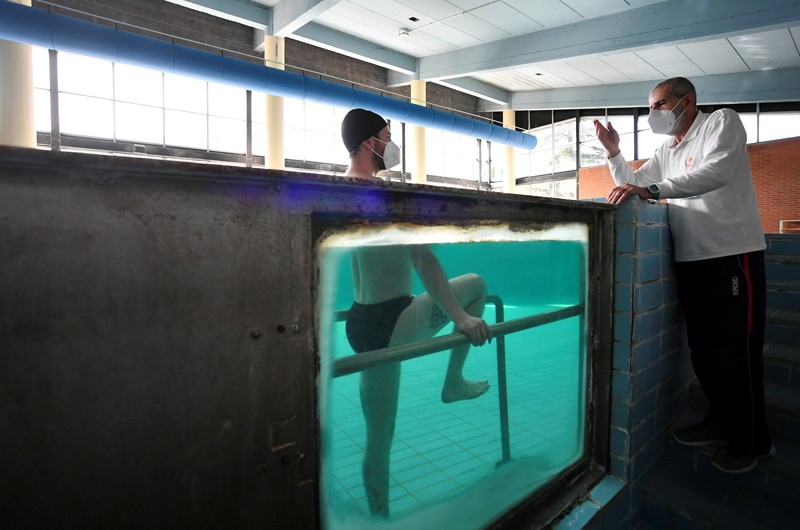 Through a window in the side of a swimming pool, a patient can be seen under water exercising on parallel bars
