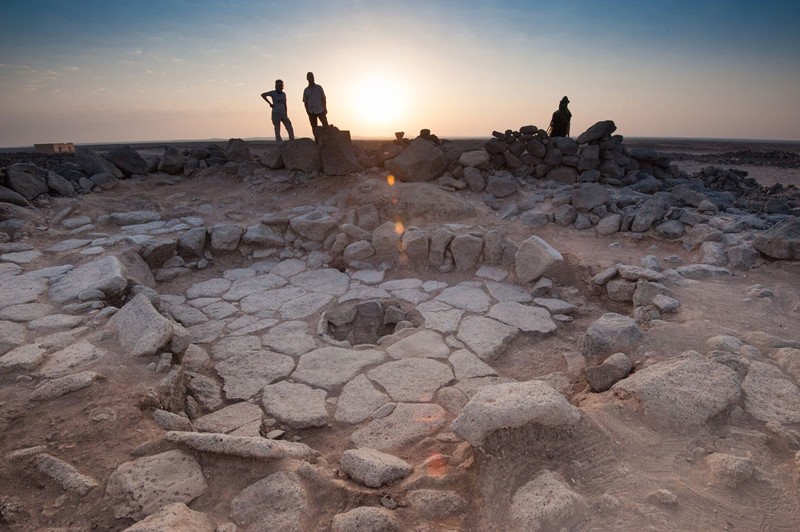 As pessoas ficam ao redor de uma estrutura circular de pedra com um fosso central no sítio arqueológico Shubayqa 1 na Jordânia