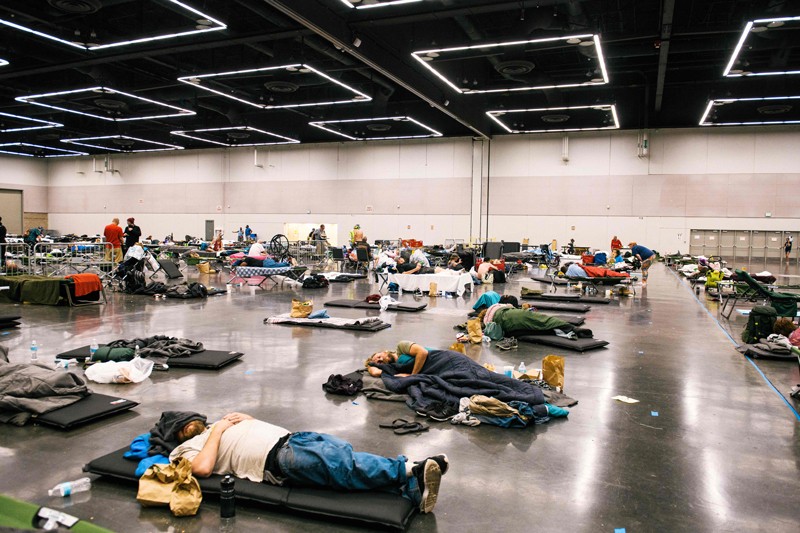 People sleep on mattresses on the floor of a large hall under ceiling fans at a cooling centre in Oregon during a heat wave