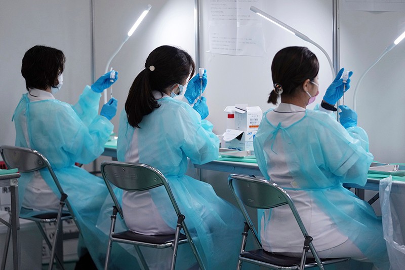 Three health workers fill syringes with the Moderna COVID-19 vaccine at a vaccination center in Tokyo.