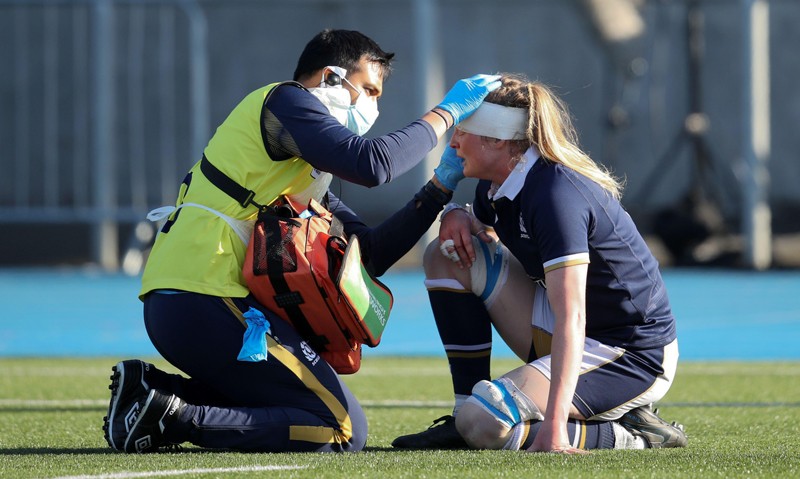 Kneeling on the pitch, a player receives treatment for a head injury from a medic during a Women's Six Nations match in 2021