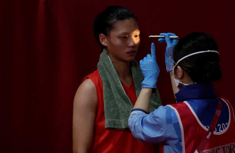 A doctor shines a torch in the eyes of an athlete competing in the women's light boxing at the Tokyo 2020 Olympic Games