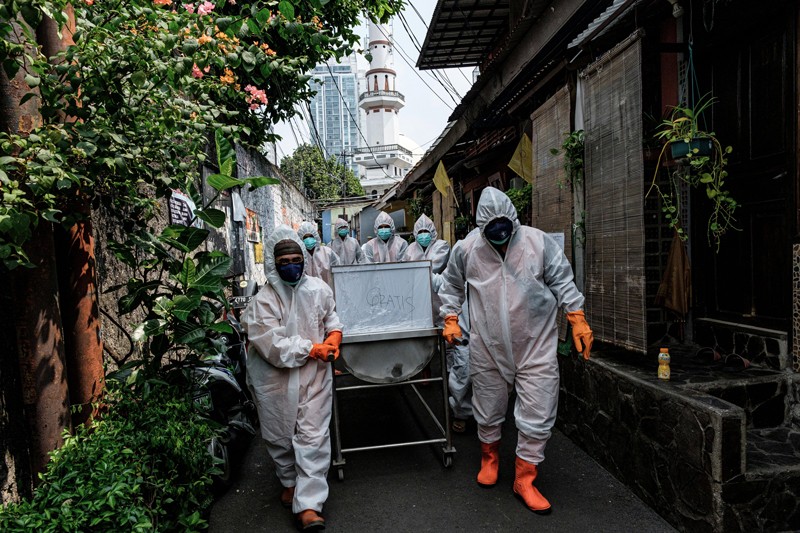 Government health workers wearing white overalls and orange boots and gloves carry a casket through the streets of Jakarta