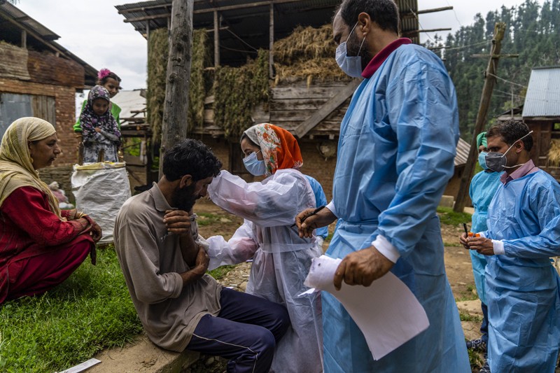 Outside a barn, a medical team in scrubs and face coverings administer a COVID-19 vaccine a resident of an Indian village