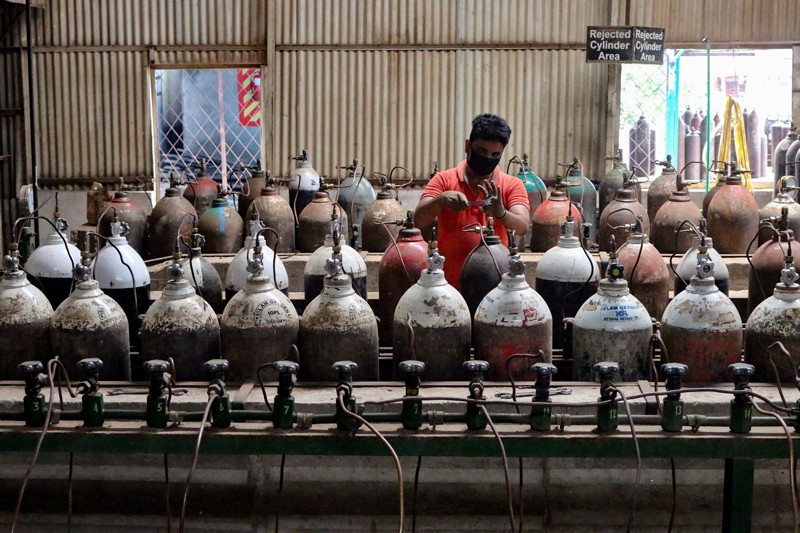 A worker in a face mask standing between rows of oxygen tanks in a factory in Bangladesh