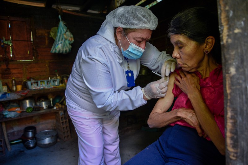 A healthcare worker administers a dose of COVID-19 vaccine to an elderly woman in her home in rural Colombia