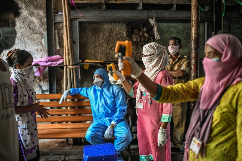 Health workers use hand held infrared thermometers to check resident's temperatures in a slum in Mumbai