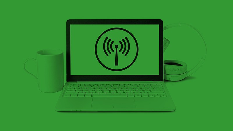 A laptop with a mug and earphones next to it on a green background.