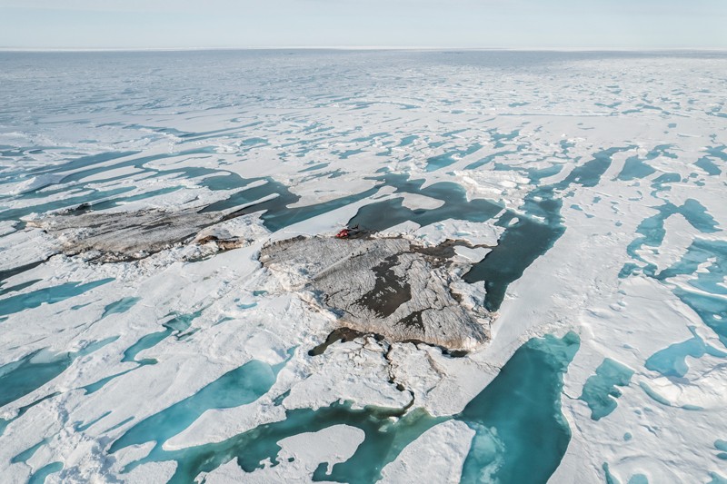 Aerial view of a small island surrounded by partially melted ice with a helicopter on it.