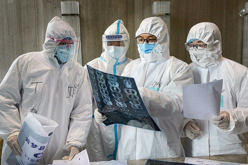 Four doctors in protective gowns look at a scan