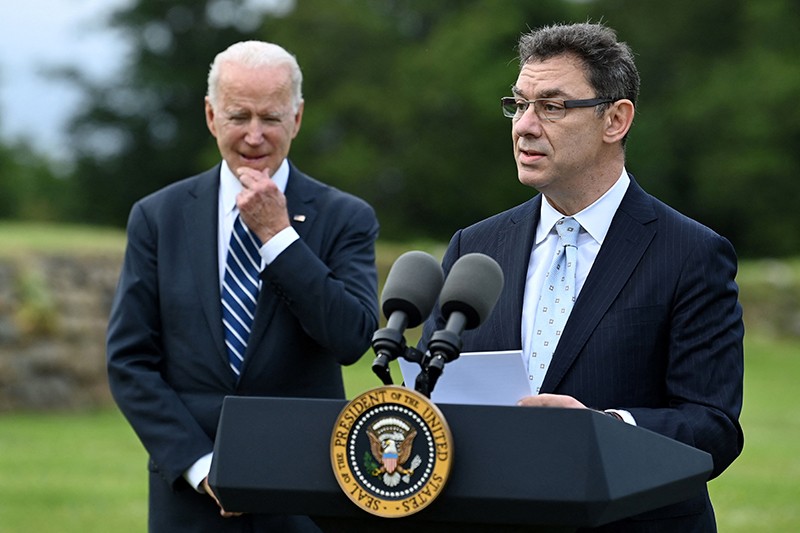 Albert Bourla speaks into microphones at a podium with Joe Biden next to him.