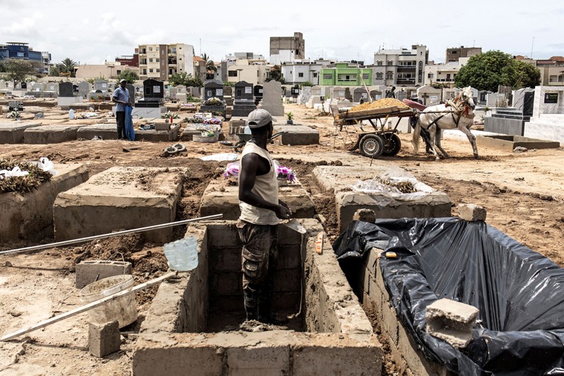 A man standing in a grave looks on as a horse-cart drops off soil to build new graves in a cemetery in Dakar