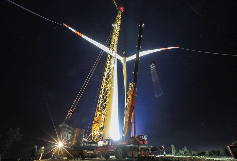 A wind turbine is erected using a crane at night