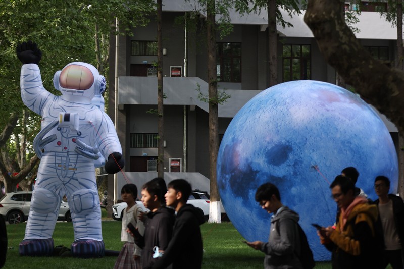 在南京航空航天大学的一个场景中，学生们走过充气宇航员和行星