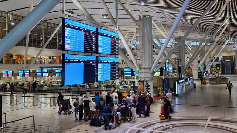 Passengers wait and look at a flight board in an otherwise empty terminal.