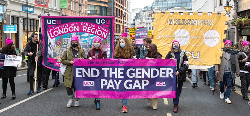 UK academics strike by walking on the streets holding signs demanding equal pay.