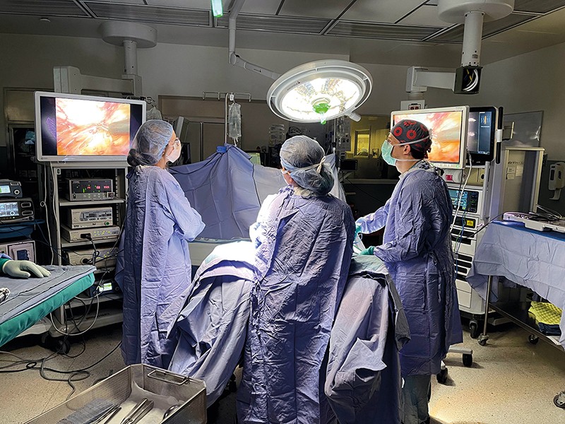 A surgical team in gowns stands around a patient in an operating theatre