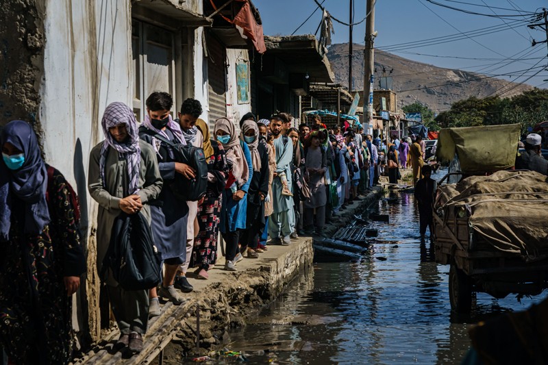 People making their way to the airport move in single file through a flooded street in Kabul, Afghanistan
