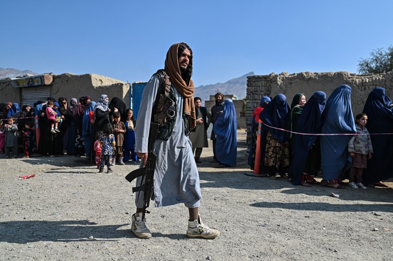 並んで待っている女性の隣を歩いているタリバン戦士