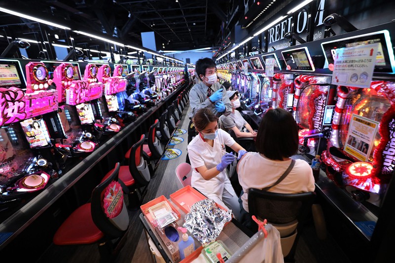People sitting in an aisle of mechanical arcade games are given vaccinations.
