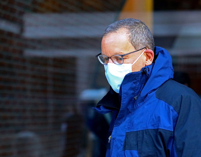 Profile image of a man in a blue coat and a face mask, walking outside.