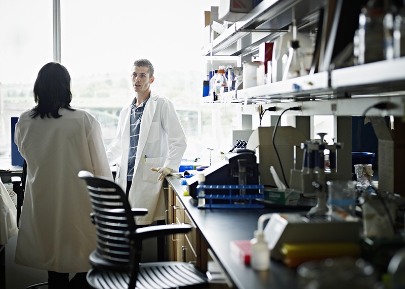 Two researchers in lab coats in discussion in a research lab.