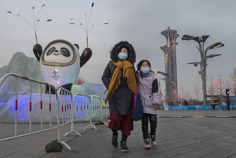 A woman and child wear protective masks as they walk by mascot Bing Dwen Dwen outside the Beijing 2022 Winter Olympics "bubble".