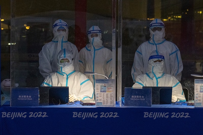 Officials wearing personal protective equipment wait to validate Olympic accreditation for people arriving at Beijing's airport.