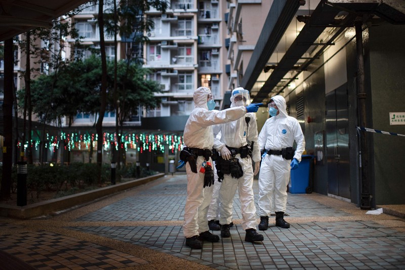 Health workers in protective overalls stand outside a building placed under lockdown in Hong Kong during the omicron wave
