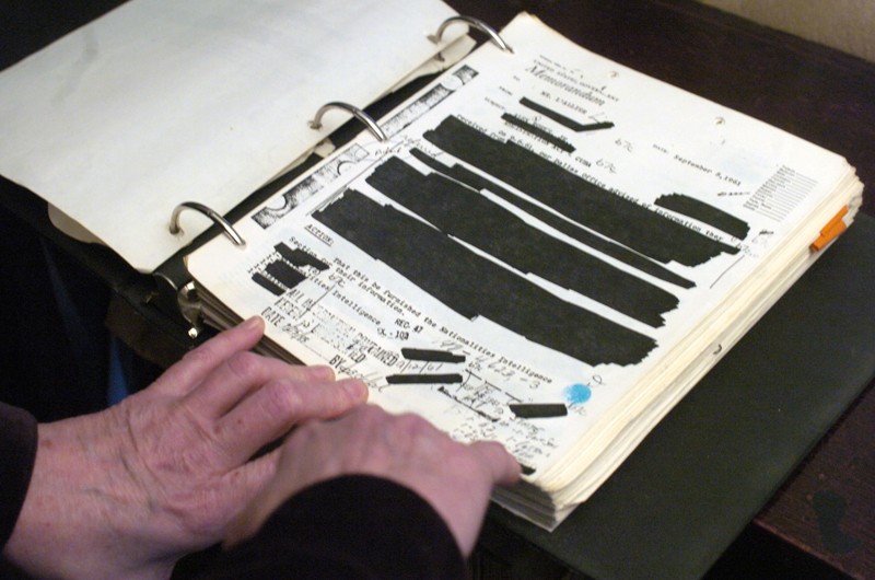 A binder of heavily hand-redacted documents