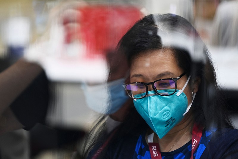 Eine Person hinter Plexiglas trägt eine Gesichtsmaske über Mund und Nase.