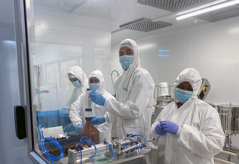 Four workers wearing personal protective equipment in a clean-room lab.
