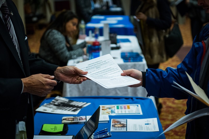 A job seeker hands a resume to a recruiter at a job fair.