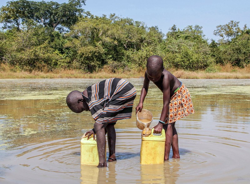 Two children in Sudan collect water from a pond using filters to remove guinea worm larvae