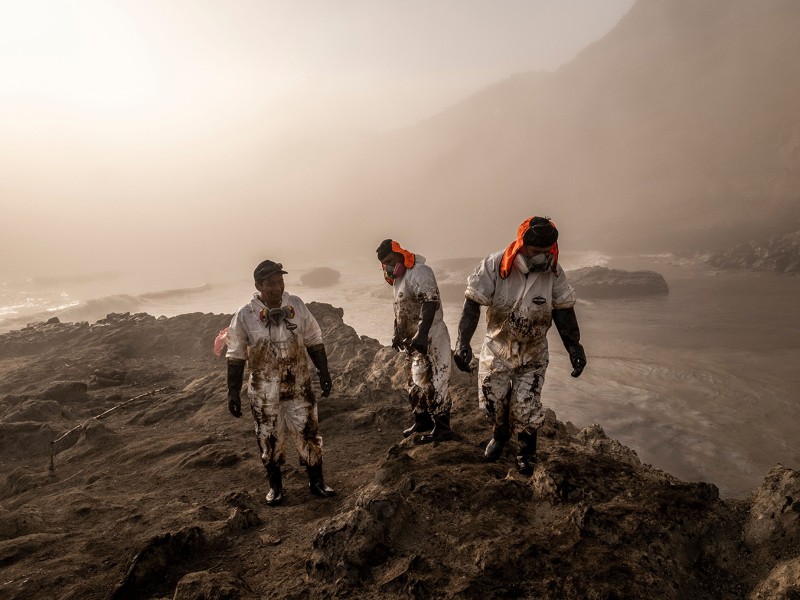 Three workers in protective suits clean up large amounts of oil washing ashore on the coastline of Peru.