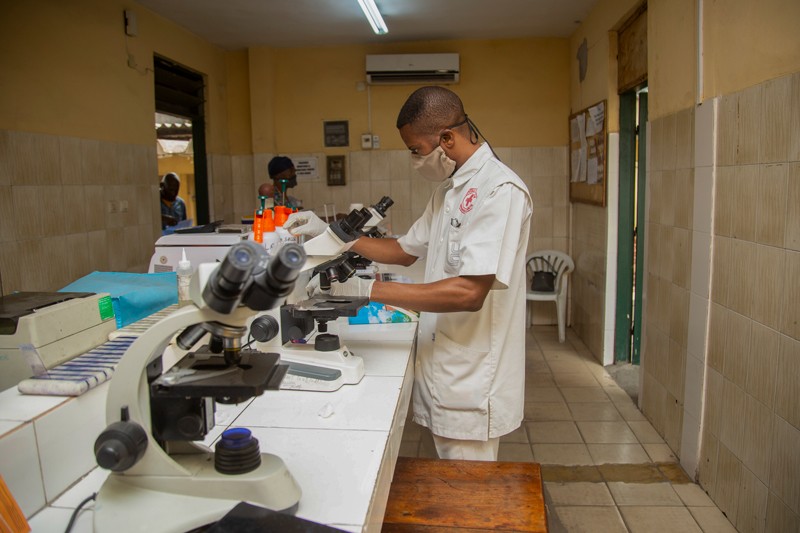 A health-care worker in a hospital in Kinshasa examining samples from COVID-19 patients under a microscope