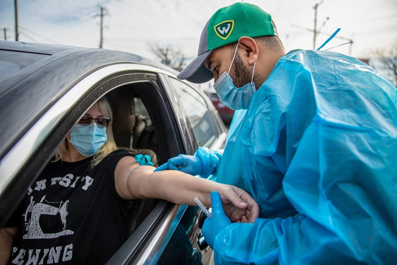 A nurse in PPE administers a monoclonal antibody treatment to a patient through her car window