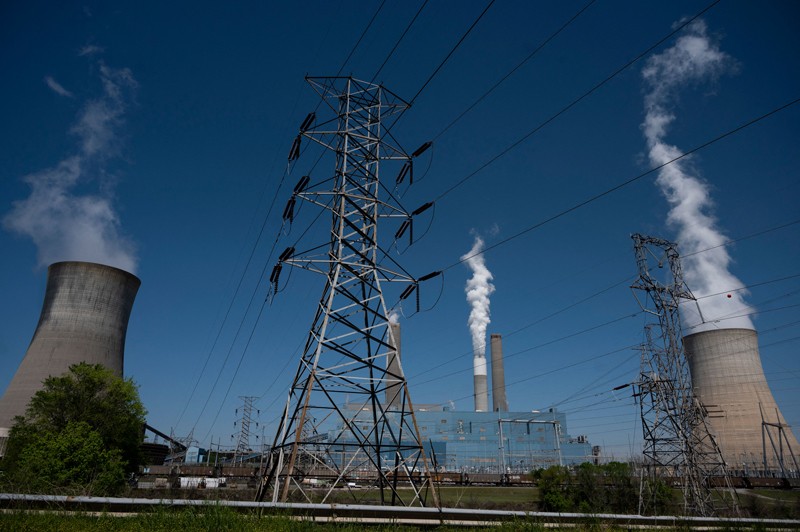 An electricity pylon stands in the middle of chimneys and cooling towers emitting steam at a coal power plant in Alabama