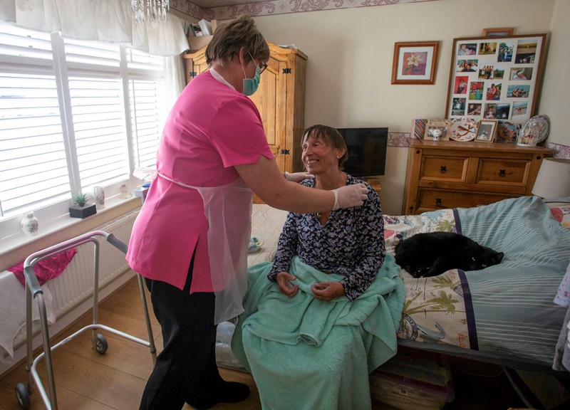 A care worker tends to a client suffering with multiple sclerosis at her home