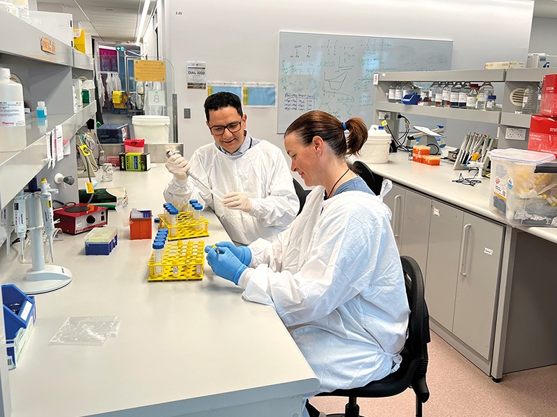 Jason Behary and colleague sit at a lab bench working with pipettes