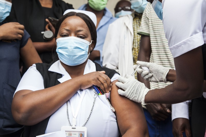 A woman wearing a nurse's uniform and mask receives a vaccine.